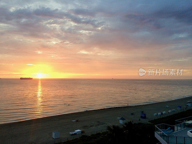 橘黄色日落/日出在美丽的迈阿密南海滩:宁静的沙滩，油轮在地平线上，太阳躺椅，云彩在紫色的天空